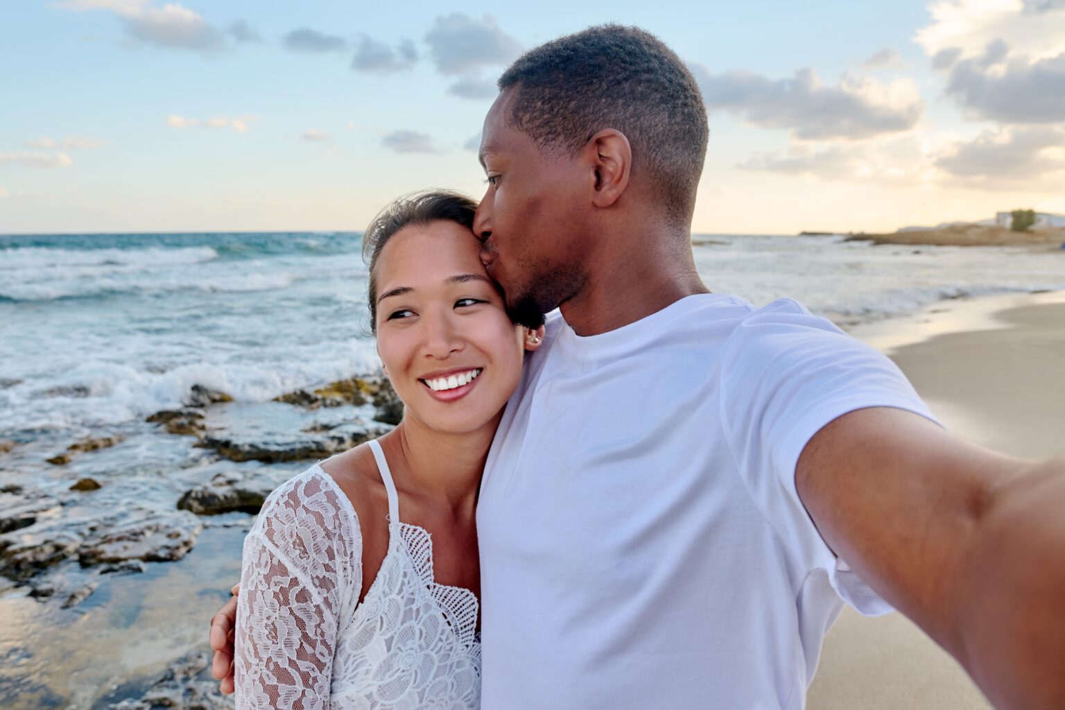 Happy couple in love kissing taking selfie together on smartphone, on beach